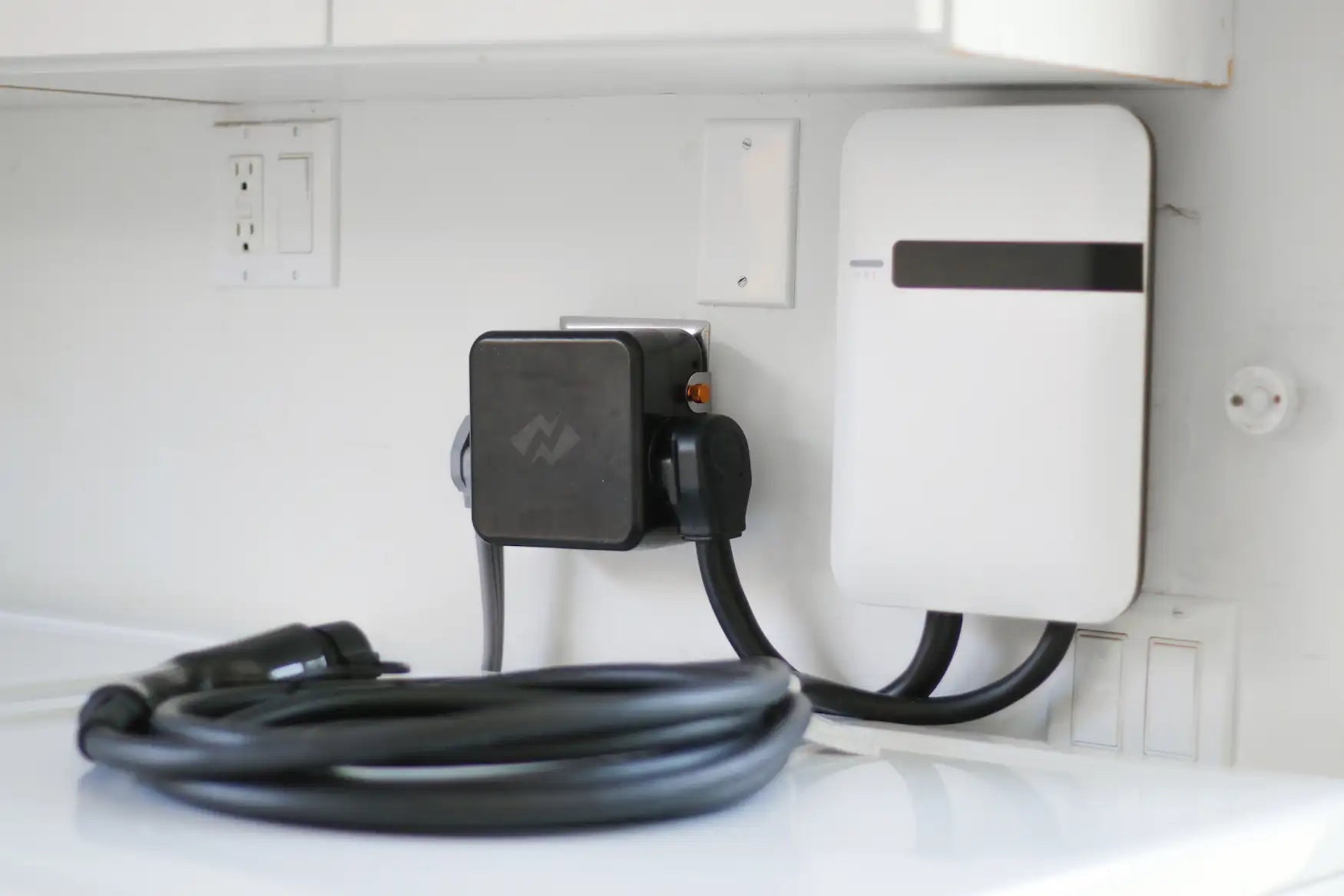 NeoCharge Smart Splitter installed on a laundry-room wall with charging cable connected to a Level 2 EV charger.