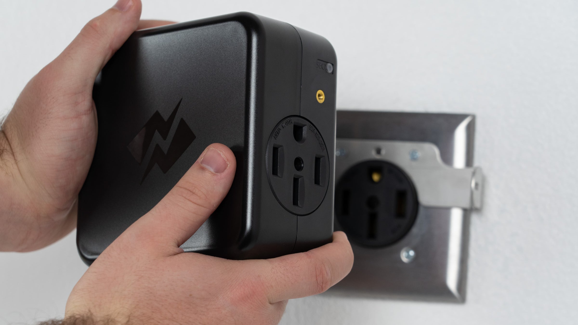 Hand holding the NeoCharge Smart Splitter against a 14-50 wall outlet during a residential install.