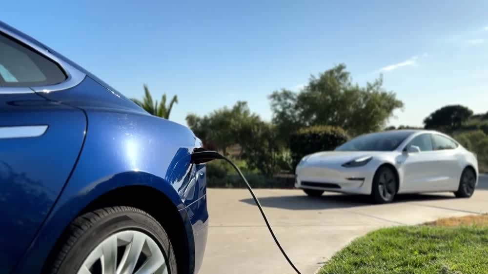 A person plugging a charging cable into a white Tesla in a driveway